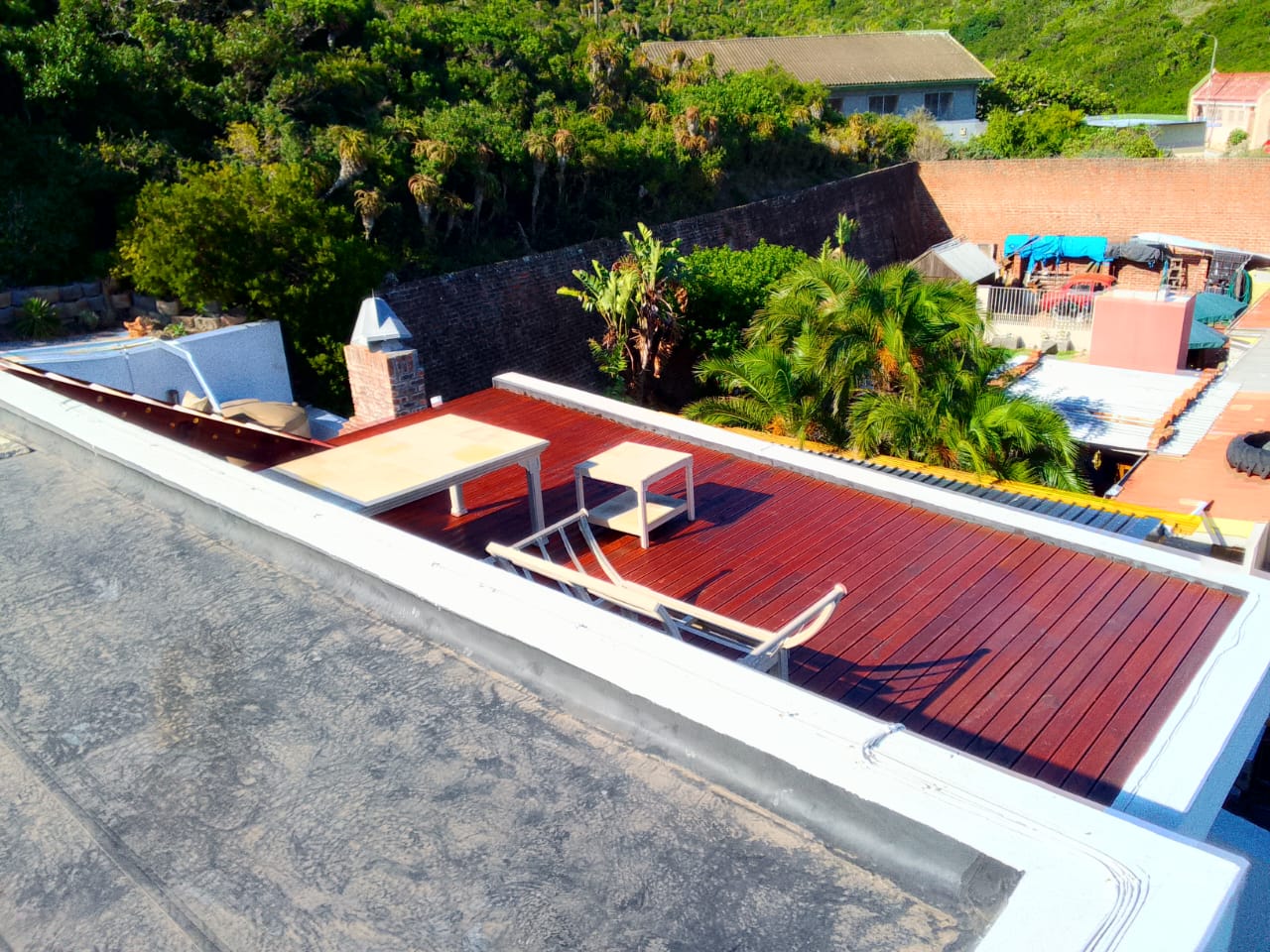 Wooden decking Port Elizabeth — completed rooftop deck stained rich mahogany red with two recliner chairs, seafront property
